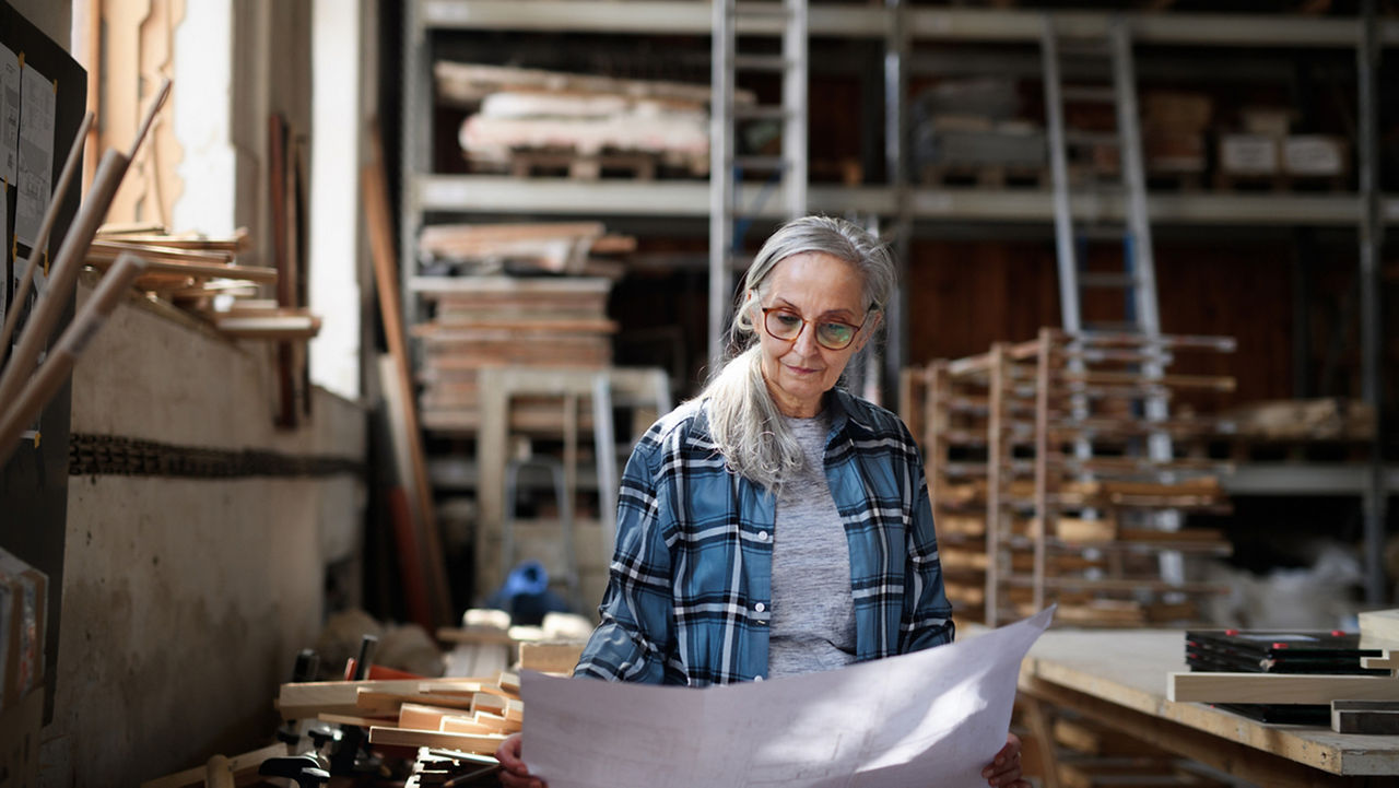 An older woman with glasses looking down at some paper in a workspace