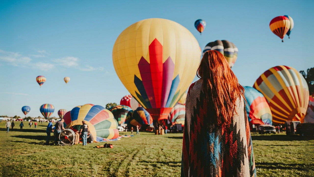Person seen from behind looking at hot air balloons floating in the sky.