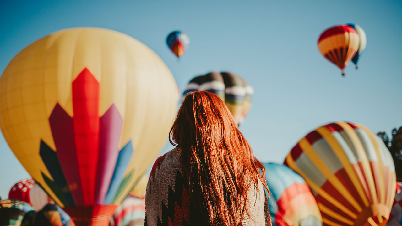 Person seen from behind looking at hot air balloons floating in the sky.